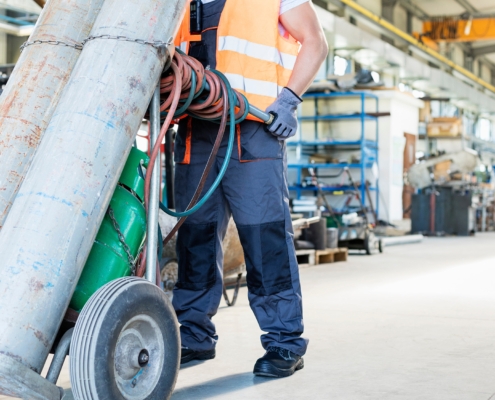 Low section of young manual worker moving gas cylinders in metal industry